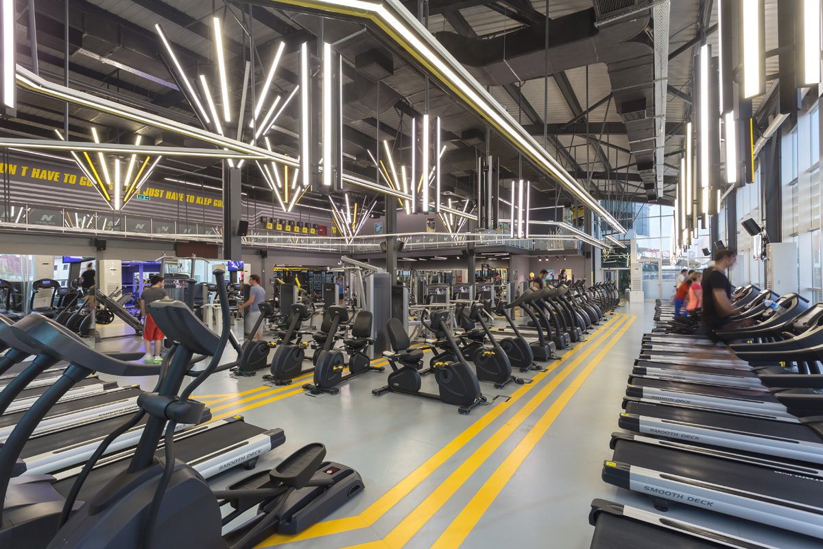 NEO LIFE Spor Merkezi fitness alanı, siyah çelik tavan, çizgisel LED armatürler ve sarı zemin çizgileri